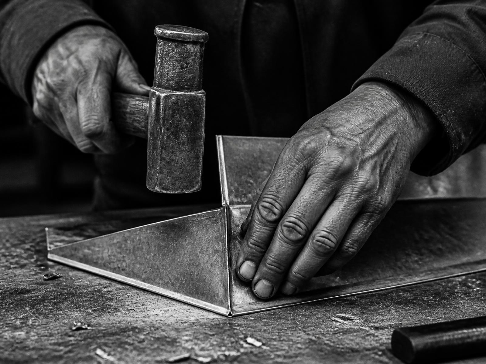 Mains d'artisan couvreur travaillant une pièce de zinc
